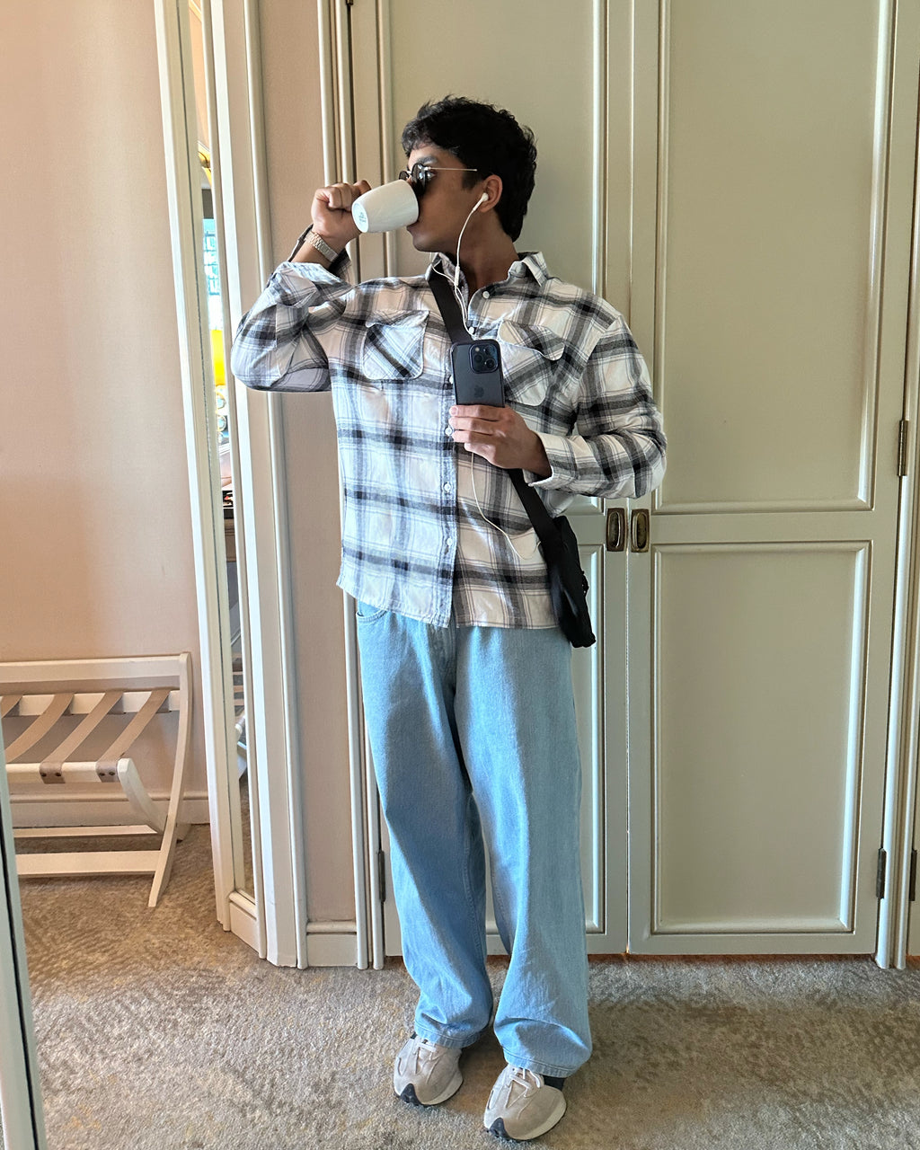 A mirror selfie of a guy wearing the white Zerodays essential flannel, well styled, listening to music using earphones and drinking coffee. 